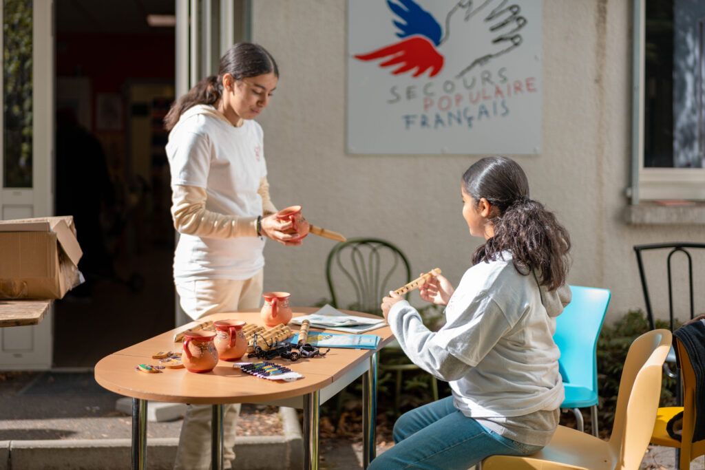 Deux Copain du Monde sont assisent devant une affiche du Secours Populaire.
