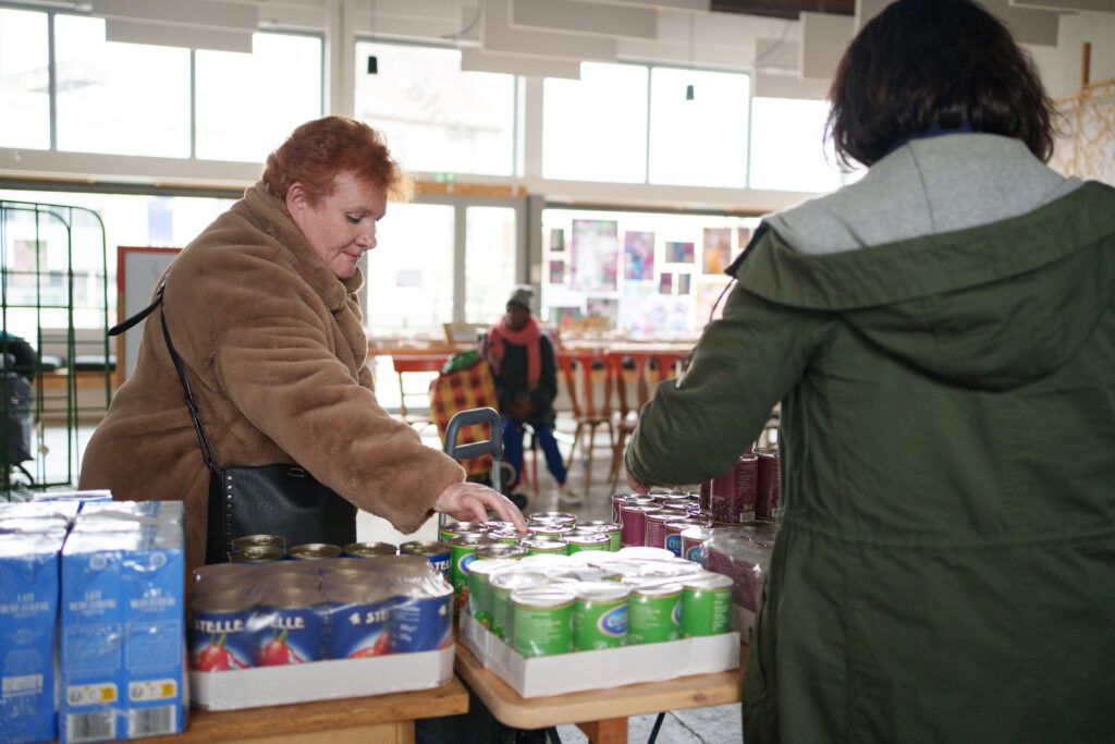 Une bénéficiaire de la distribution alimentaire choisit ses boites de conserve. Au Point Coop – Café Deux-Rives,