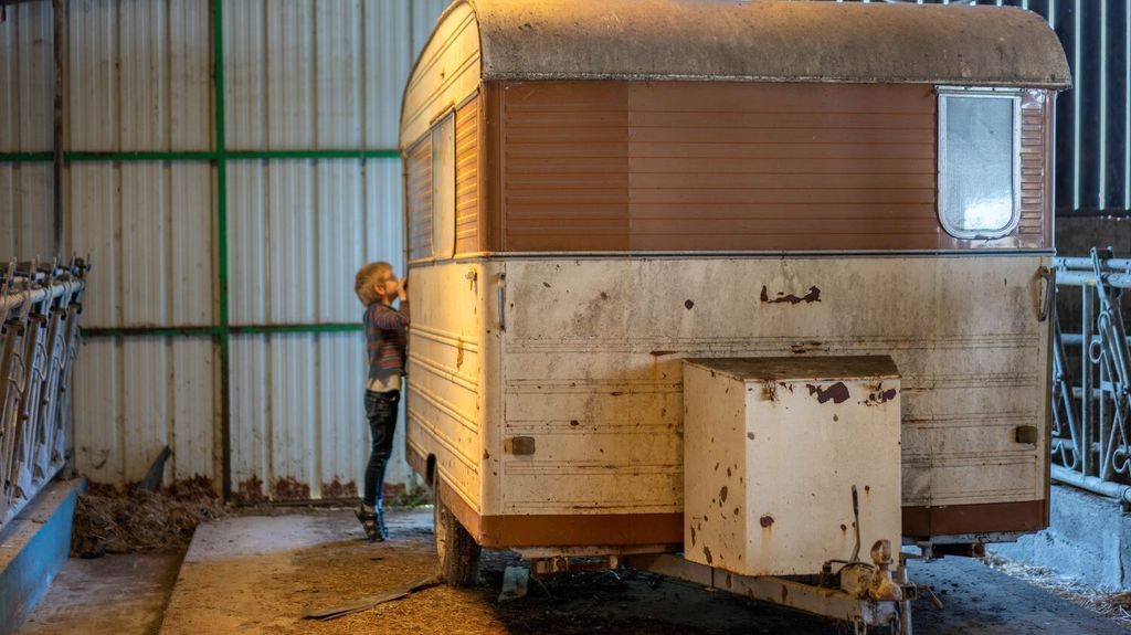Un enfant regarde à travers la vitre d'une caravane abandonnée