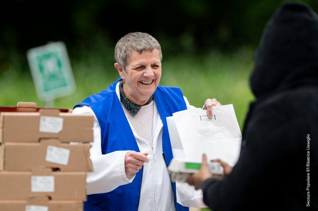 Une bénévole du Secours populaire souriante qui donne un sac à une personne aidée