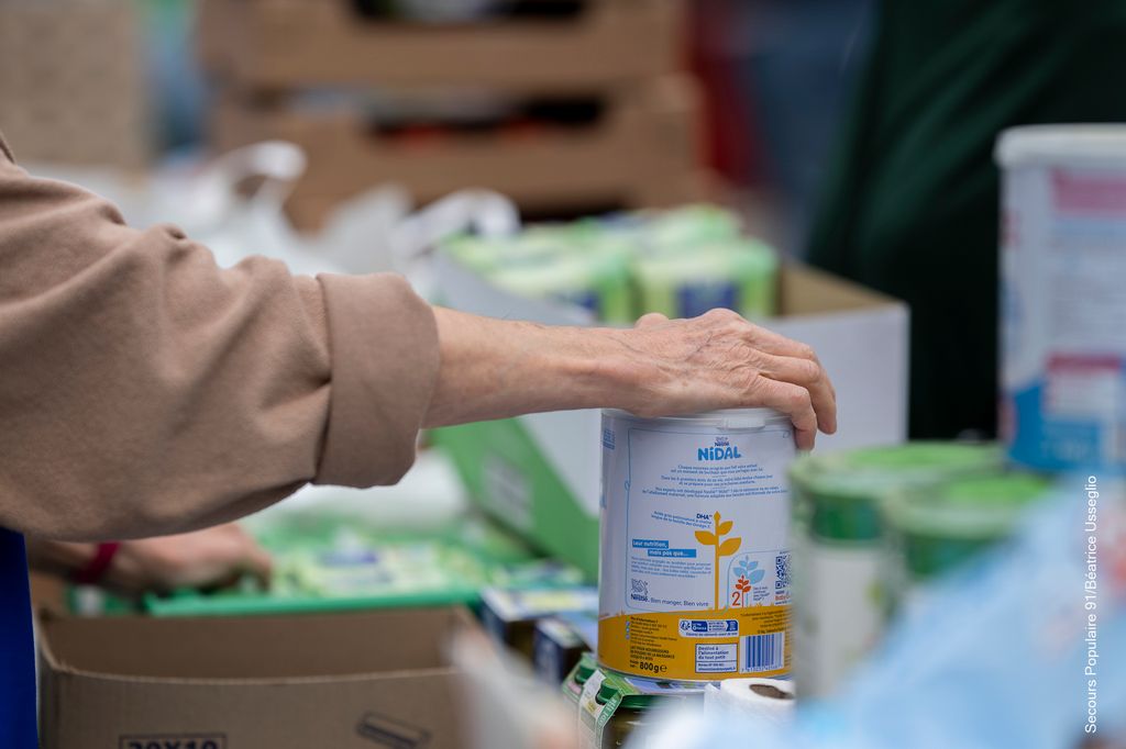 La main d'une bénévole du Secours populaire qui prend une boîte de conserve.
