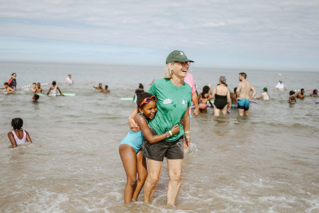 Les pieds dans l'eau, une bénévole et une petite fille se tiennent par les bras.
