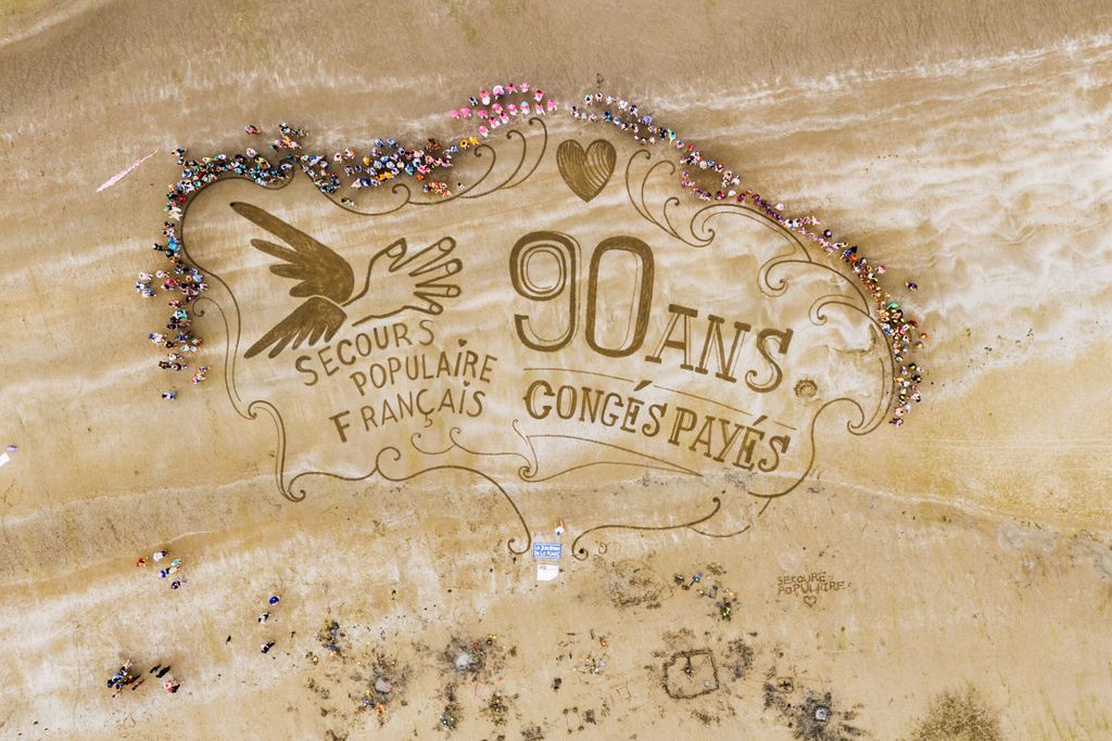 Photo prise au drone sur la plage avec les enfants qui entourent un dessin géant du logo du Secours populaire et une inscription "90 ans des congés payés"
