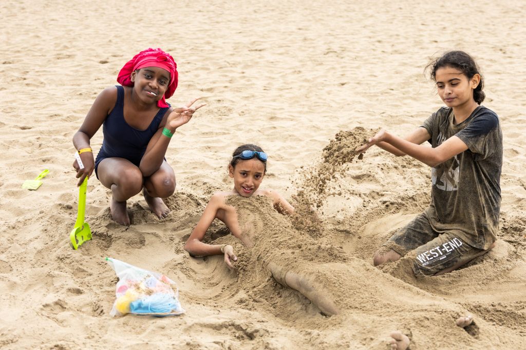 Deux enfants ensablent une camarade sur la plage.