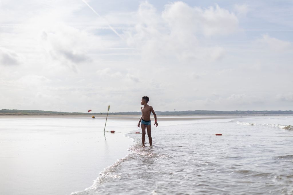 Un seul enfant au milieu de l'image, les pieds dans l'eau, avec l'impression qu'il a toute la plage pour terrain de jeu.