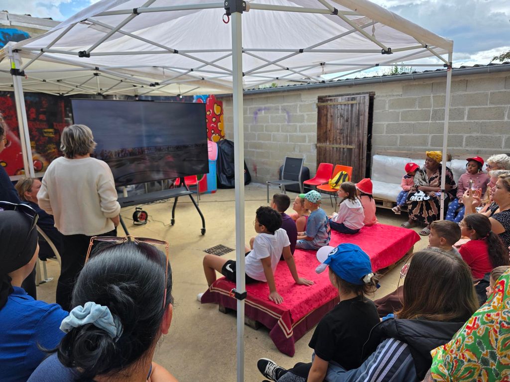 Un groupe d'enfant et leurs familles regardent une grande télévision sur laquelle sont projeté les photos de la JOV.