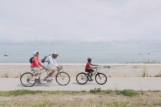 Un couple d'une soixantaine d'année fait du tandem avec un enfant à vélo au bord de la mer