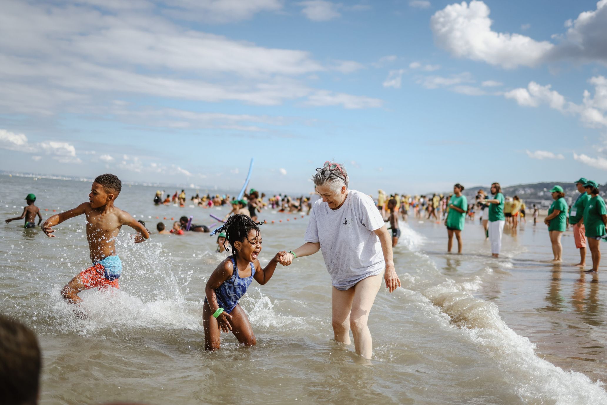 Une bénévole tient par la main une petite fille au bord de l'eau.