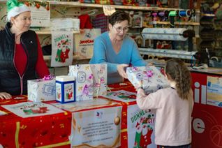 Des bénévoles Pères Noël verts donnent un cadeau emballé à une petite fille aidée par le Secours populaire.