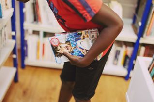 Un jeune garçon, dans une bibliothèque du Secours populaire, tient dans sa main gauche un livre de mangas.