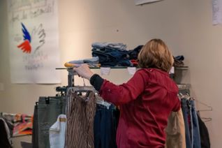 Une femme, de dos, regarde les articles proposés sur un portant par le Secours populaire français, à la recherche de bonnes affaires.