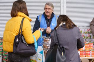 Un bénévole, de face, propose des denrées alimentaires à de jeunes étudiantes venues au Secours populaire français.