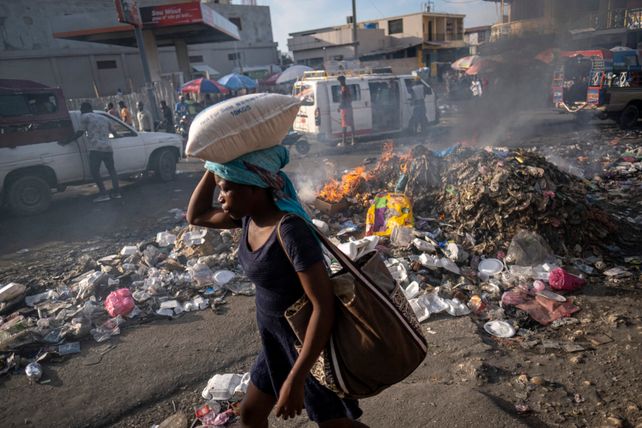 Une femme portant un sac de riz sur la tête passe devant un tas d'ordures en feu à Port-au-Prince (archive)