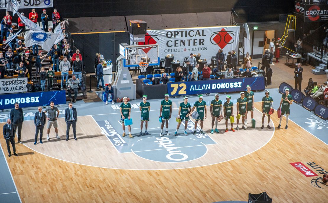 Une trentaine d’étudiants dijonnais, accompagnés par le Secours populaire, sont invités à assister au match de championnat de France de basket Dijon/ limoges le 16 décembre 2023 Les joueurs, qui portent un bonnet PNV, organisent une collecte de cadeau sur le terrain.