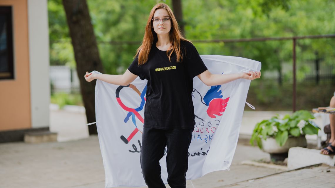 Une jeune fille brandit derrière son dos, d'un drapeau au logo des Copain du Monde.