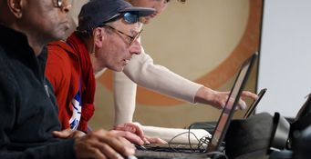 Deux personnes devant des ordinateurs écoutent le bénévole de l'atelier d’éducation au numérique du Secours populaire à Toulouse