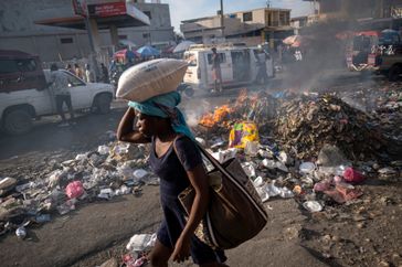 Une femme portant un sac de riz sur la tête passe devant un tas d'ordures en feu à Port-au-Prince (archive)